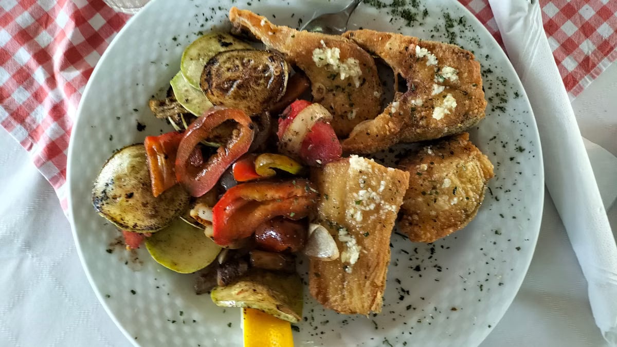 A delicious grilled fish dish with vegetables served on a white plate. Perfect meal idea.