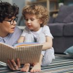 a woman reading a book to a child on the floor
