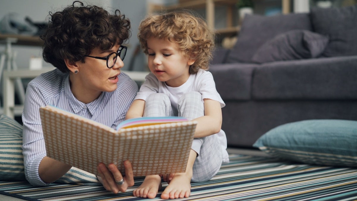 a woman reading a book to a child on the floor